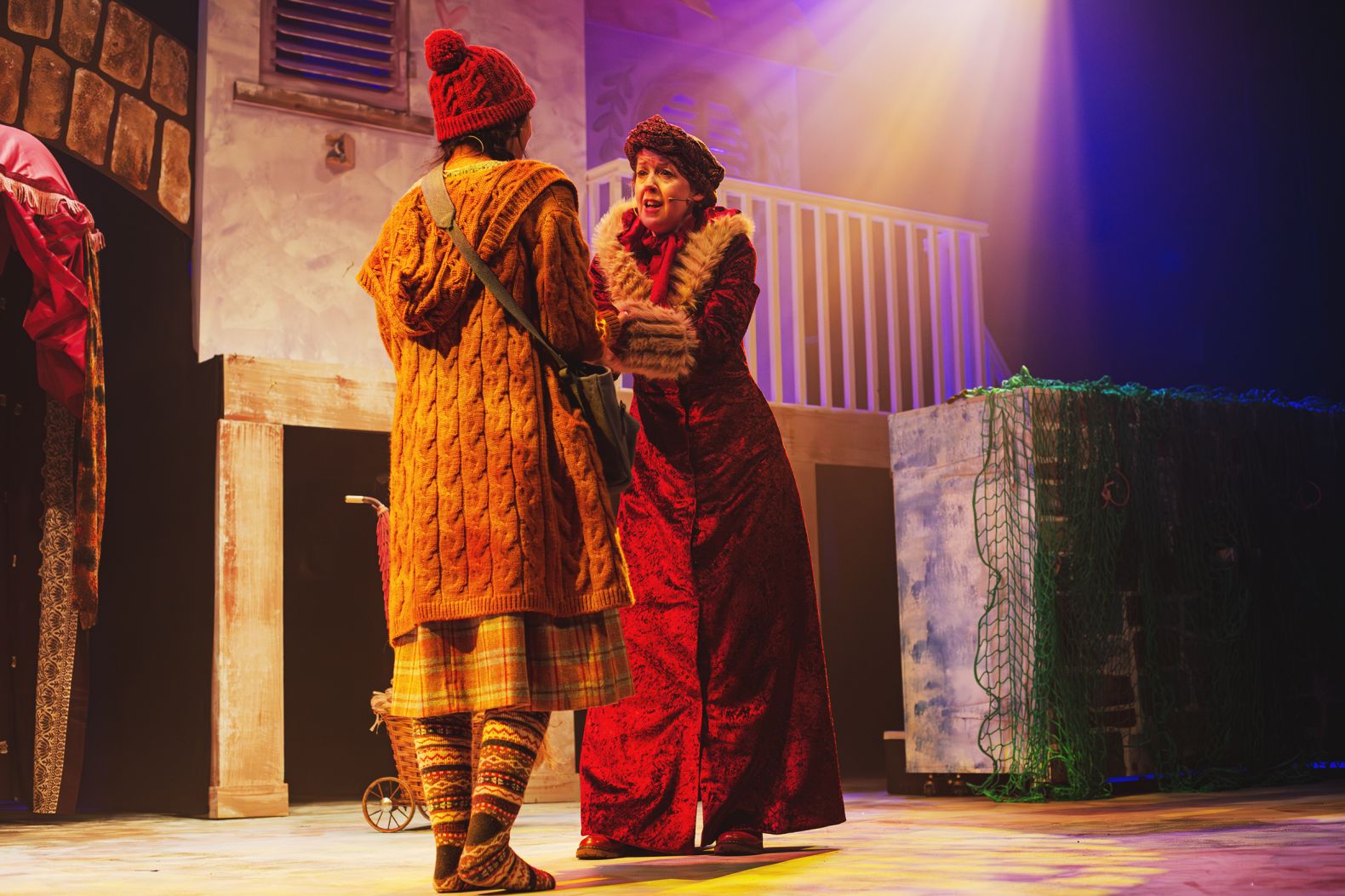 The Snow Queen at The Dukes - a magic women dressed in a full length red-velvet coat is holding the hands of Gerda who is wearing a a chunky yellow cardigan.