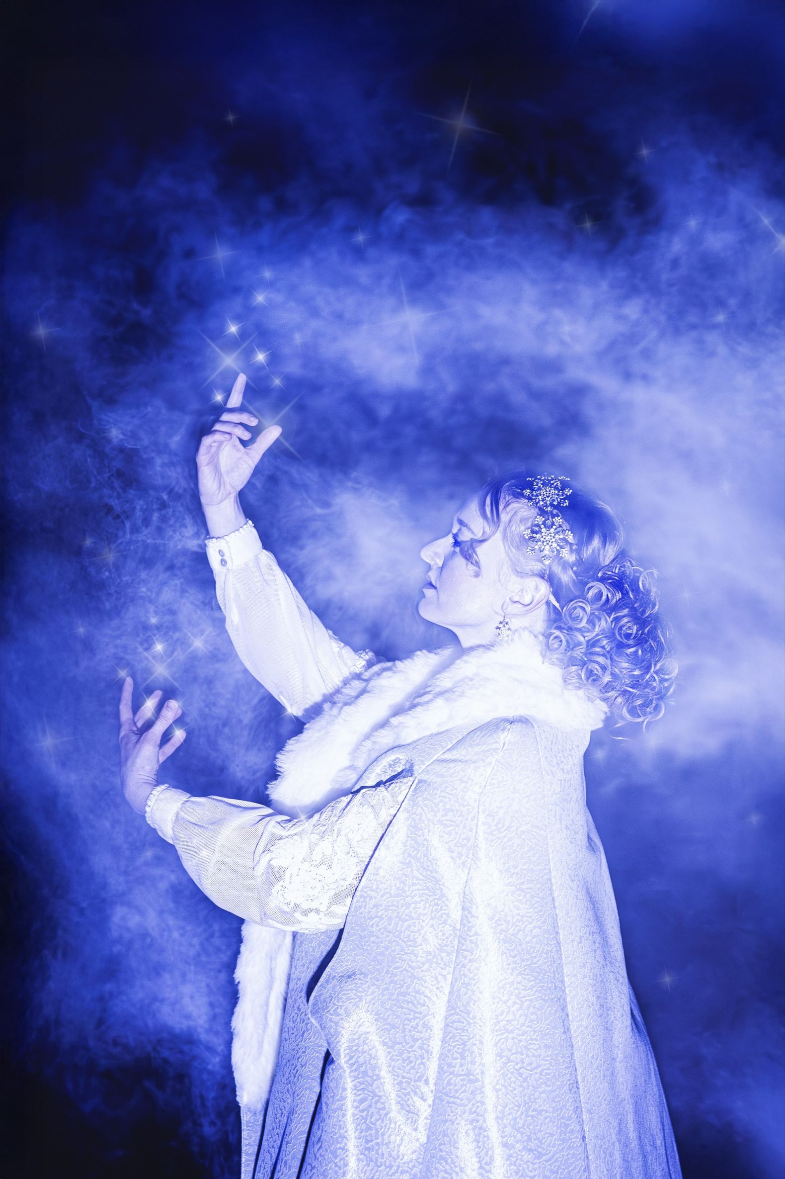 The Snow Queen at The Dukes - The Snow Queen stands in a forest and white and blue smoke swirl around her.