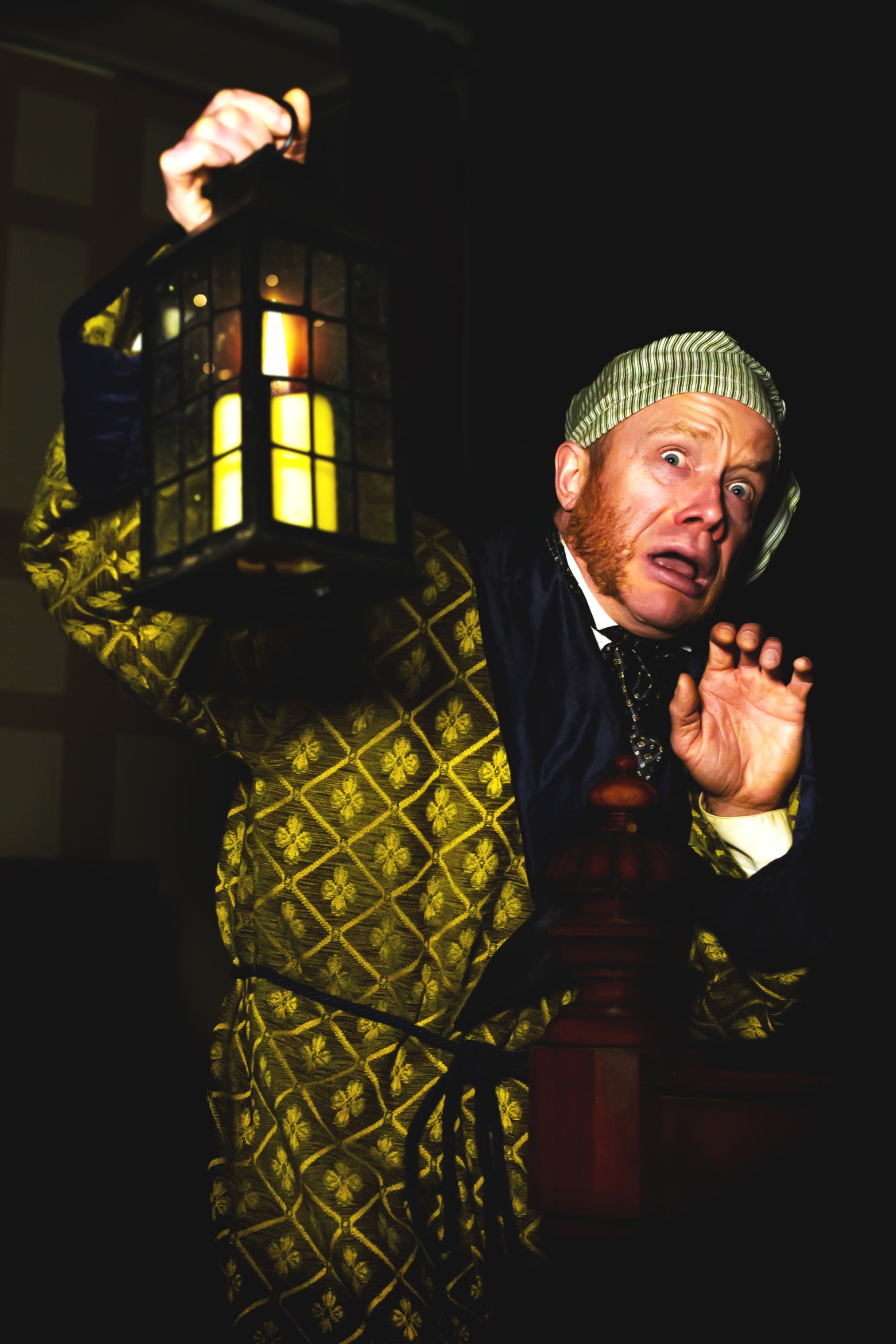 Ebenezer Scrooge in night robe holding a lantern, looking scared