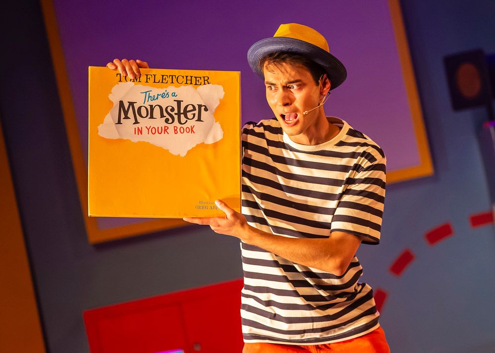 An actor holding up a book titled "There's a Monster in Your Book"