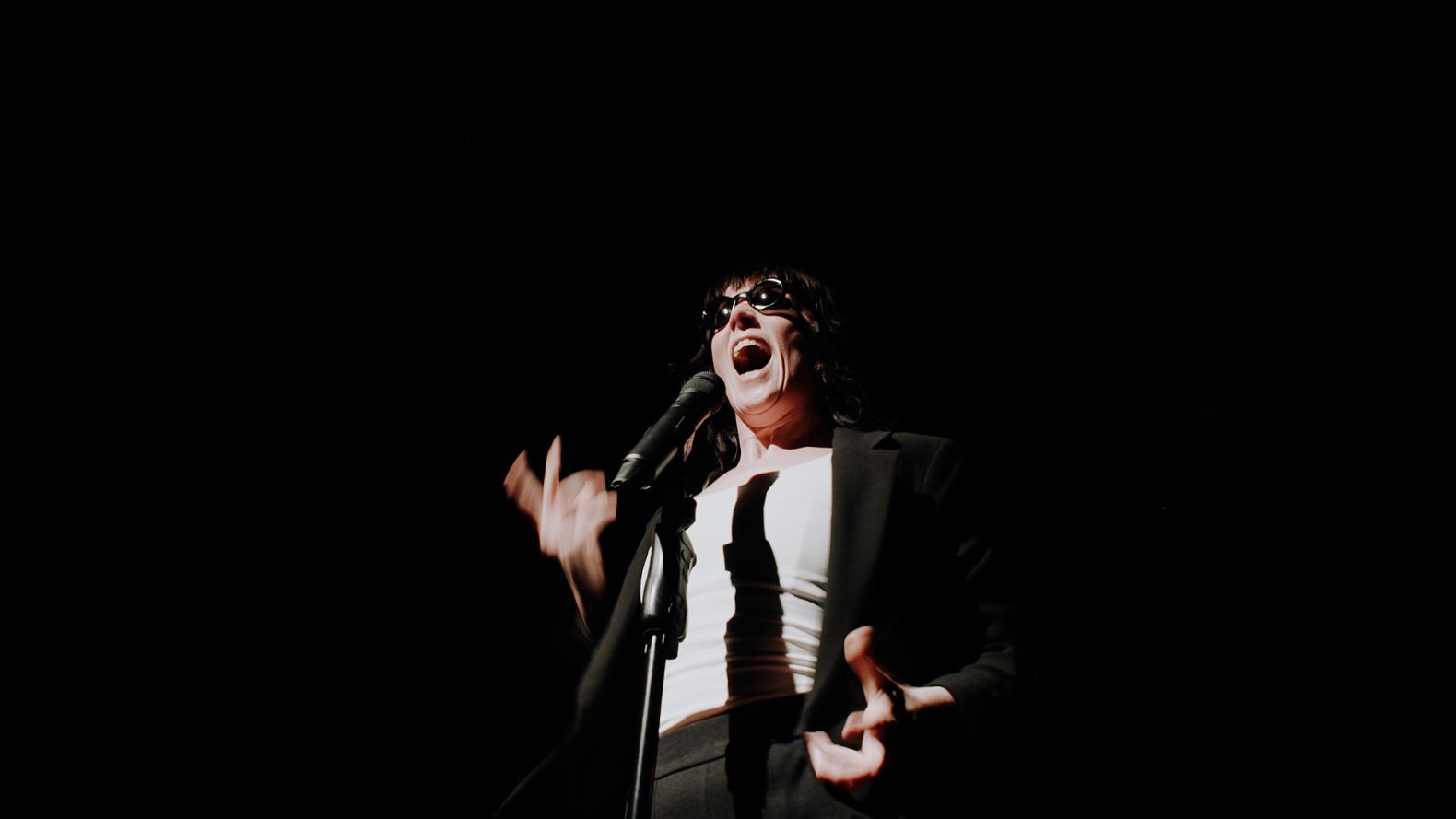 performer in black and white suit screams into microphone wearing sunglasses
