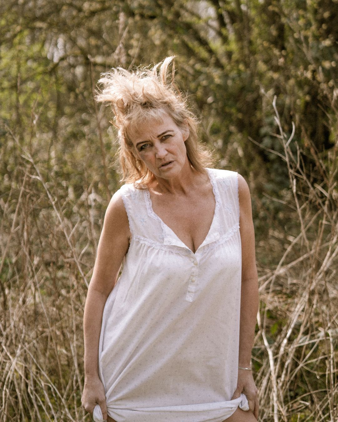 performer in a field wearing all white, their hair is messy and they're looking directly into the camera - Macbeth by HER Productions at The Dukes, Lancaster