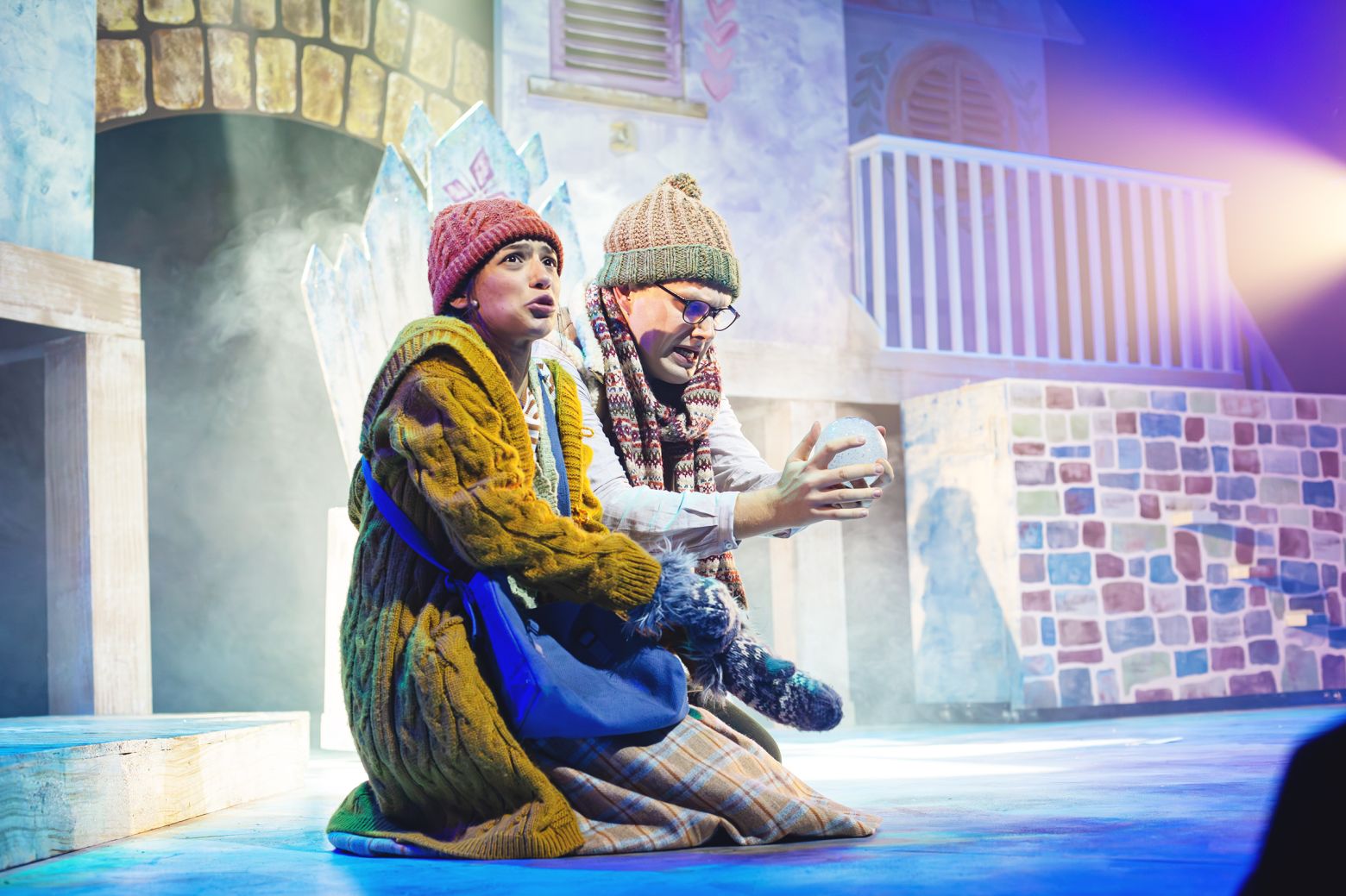 The Snow Queen at the Dukes - Gerda, in a chunky yellow cardigan and Kai, in glasses and a bobble hat are sat on the floor of the Snow Queens ice palace.