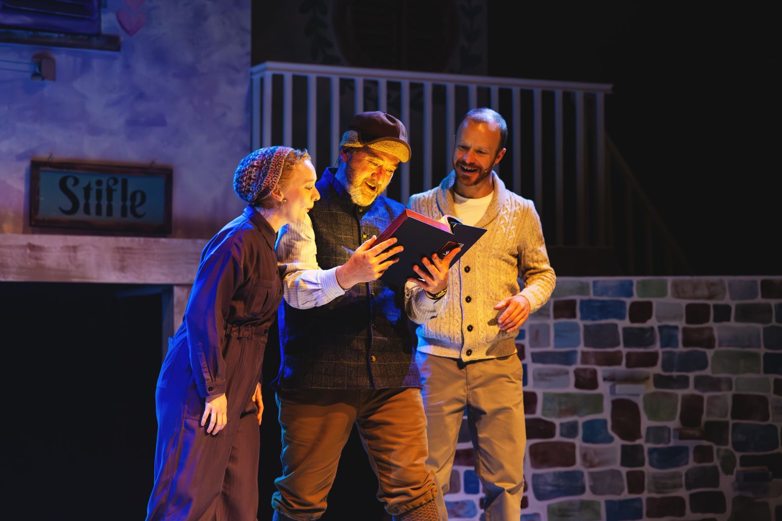 The Snow Queen at The Dukes - 3 villagers looking into a book, there is light coming from the pages that is lighting their faces.