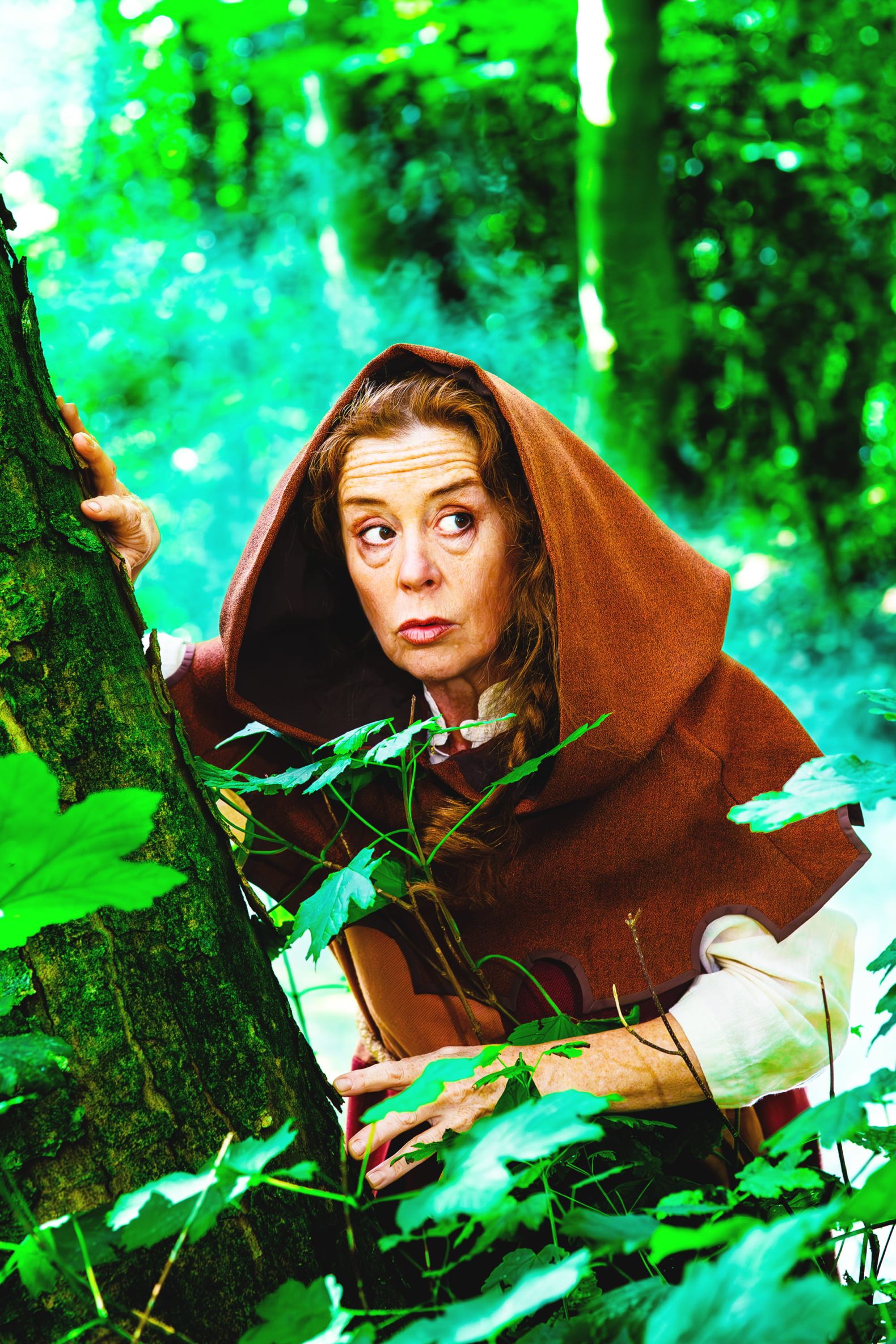 Robin Hood - the Dukes Park Show in Williamson Park: Friar Tuck peaks around a tree with her hood up and looking sneaky