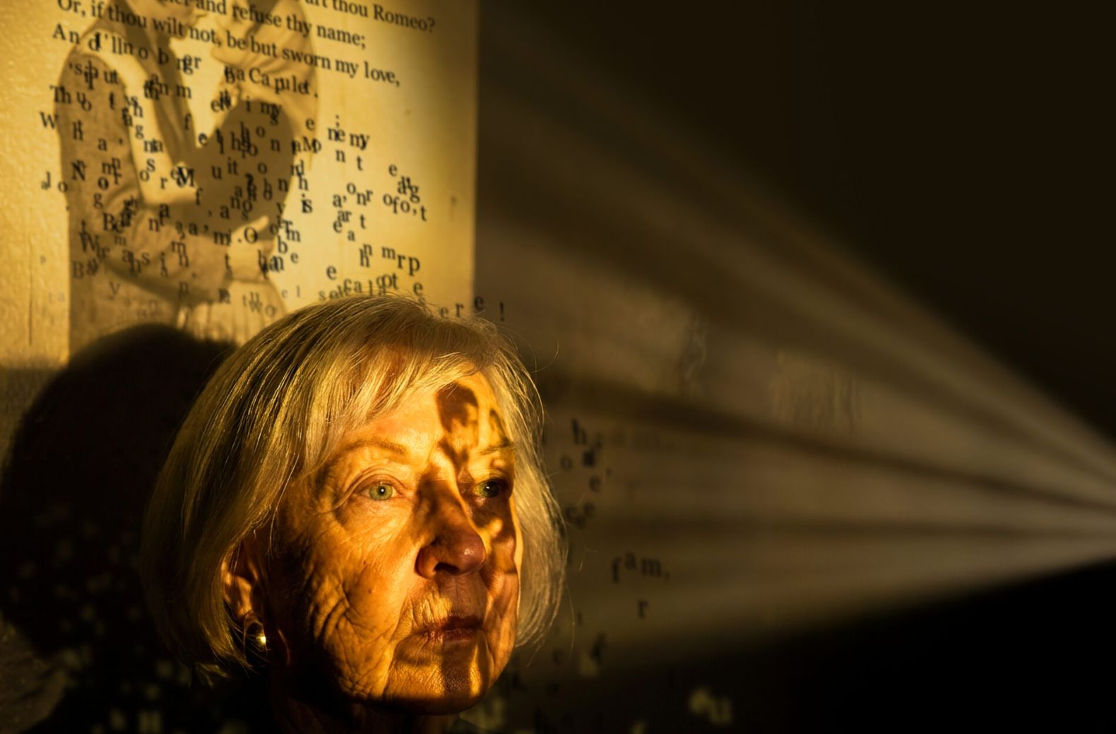 The Remember Romeo poster image: an elderly lady with the image of a younger couple embracing projected onto her face and the wall behind