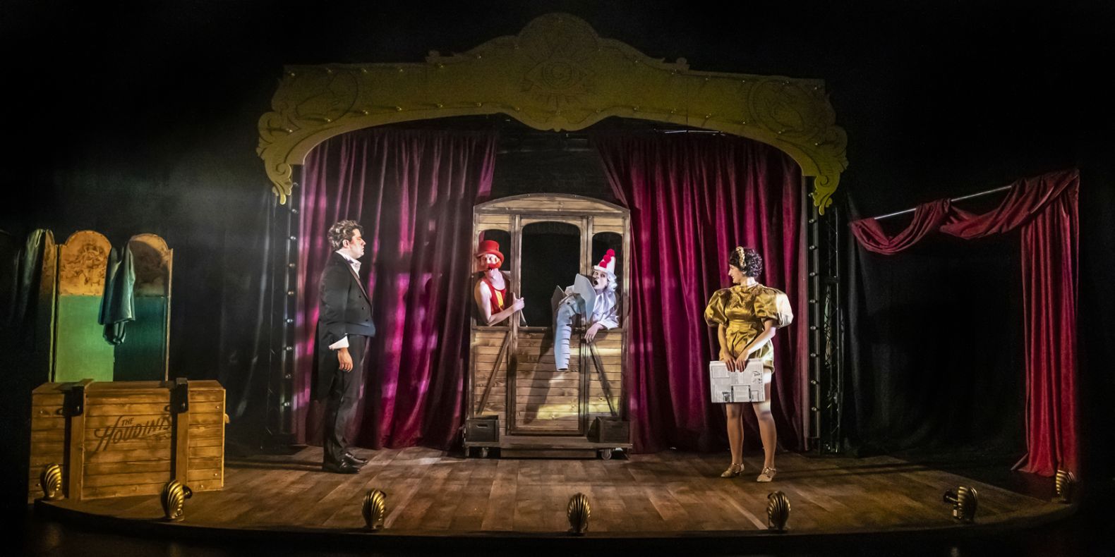 four cast members on stage with a set made up of red velvet curtains and golden footlights
