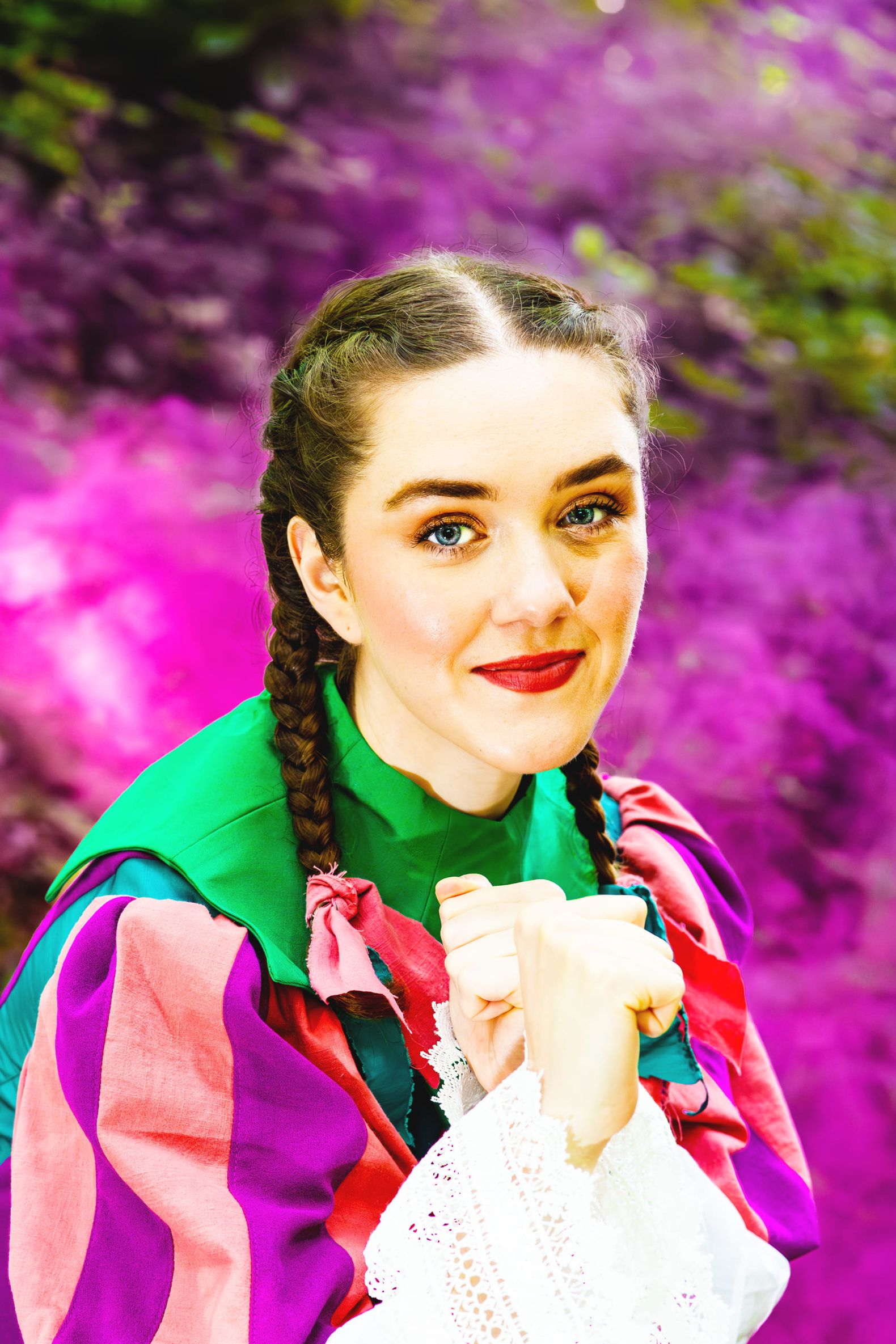 Robin Hood - the Dukes Park Show in Williamson Park: Jen stands ready to fight with fists held high, she is wearing a pink and purple dress and is surrounded by pink smoke