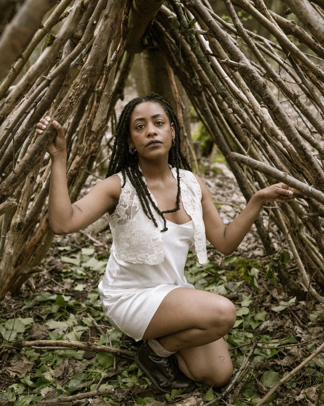 performer in white dress kneeling in a forest with branches behind them - Macbeth by HER Productions at The Dukes, Lancaster
