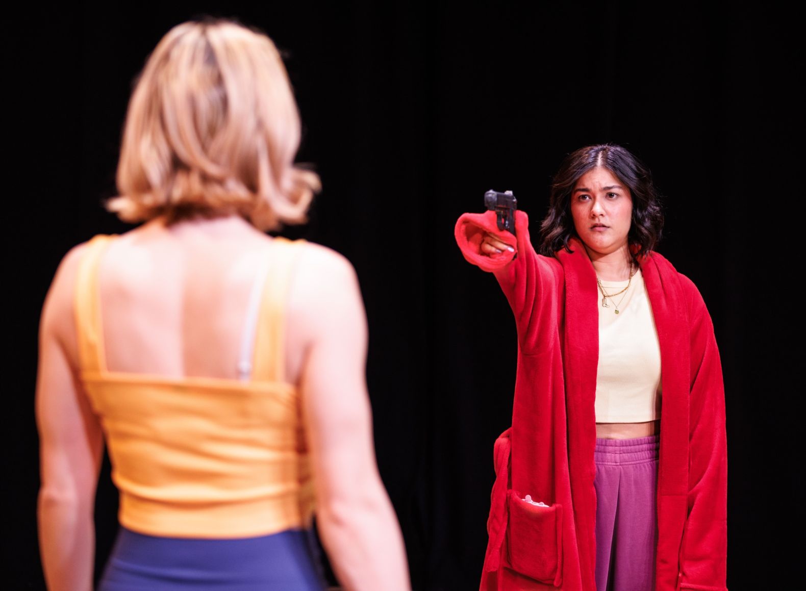 Production photo of Rotten by Emmerson & Ward - a woman in a red dressing gown is pointing a gun a young woman who has her back to camera