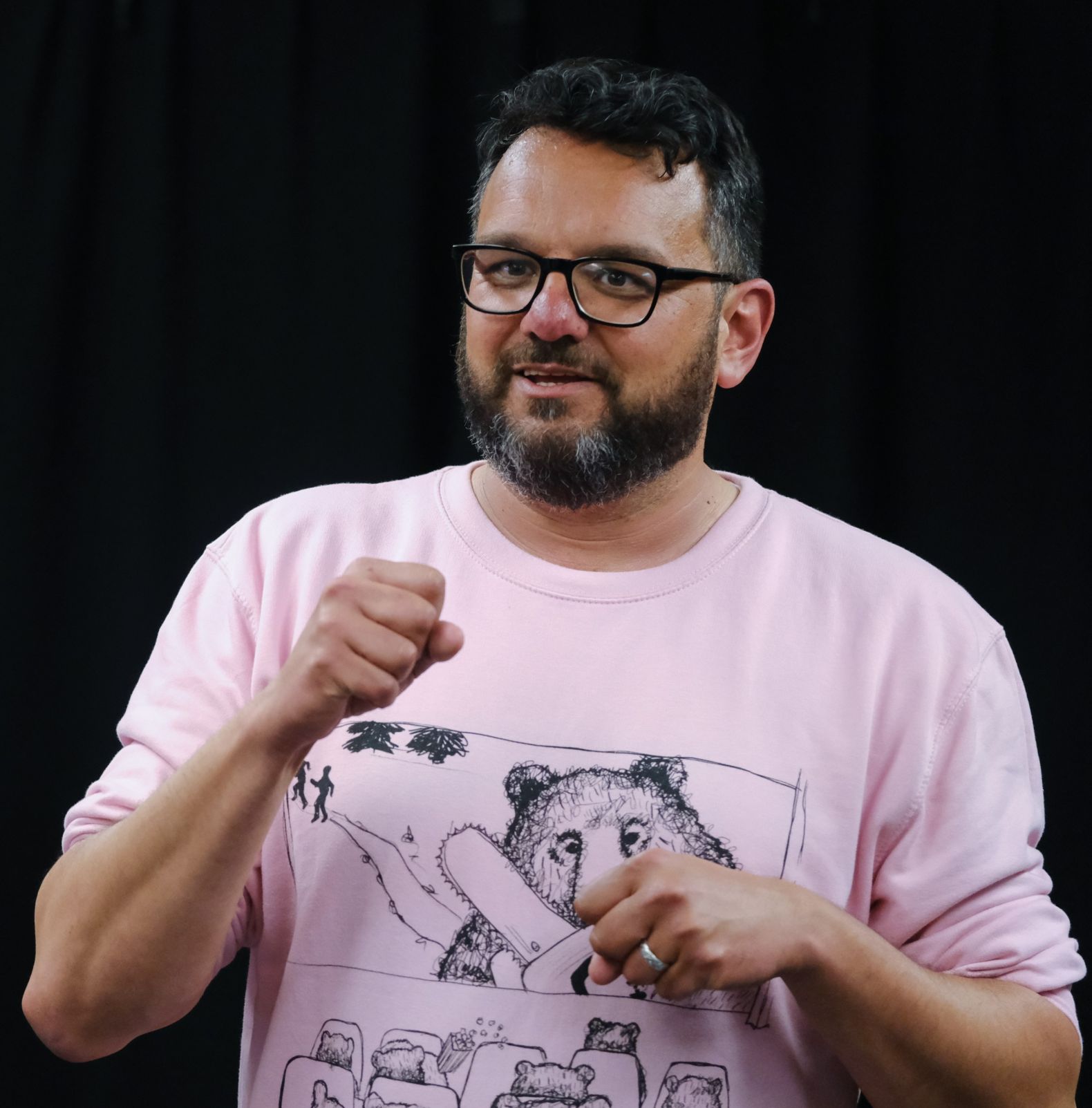 man in glasses and pink jumper talkign to camera