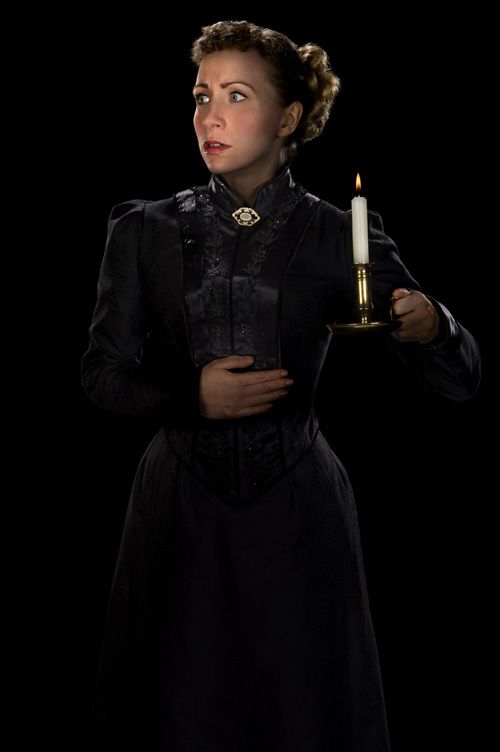 Christmas Gothic: the heroine, dressed in a black Victorian dress and holding a candle in the dark