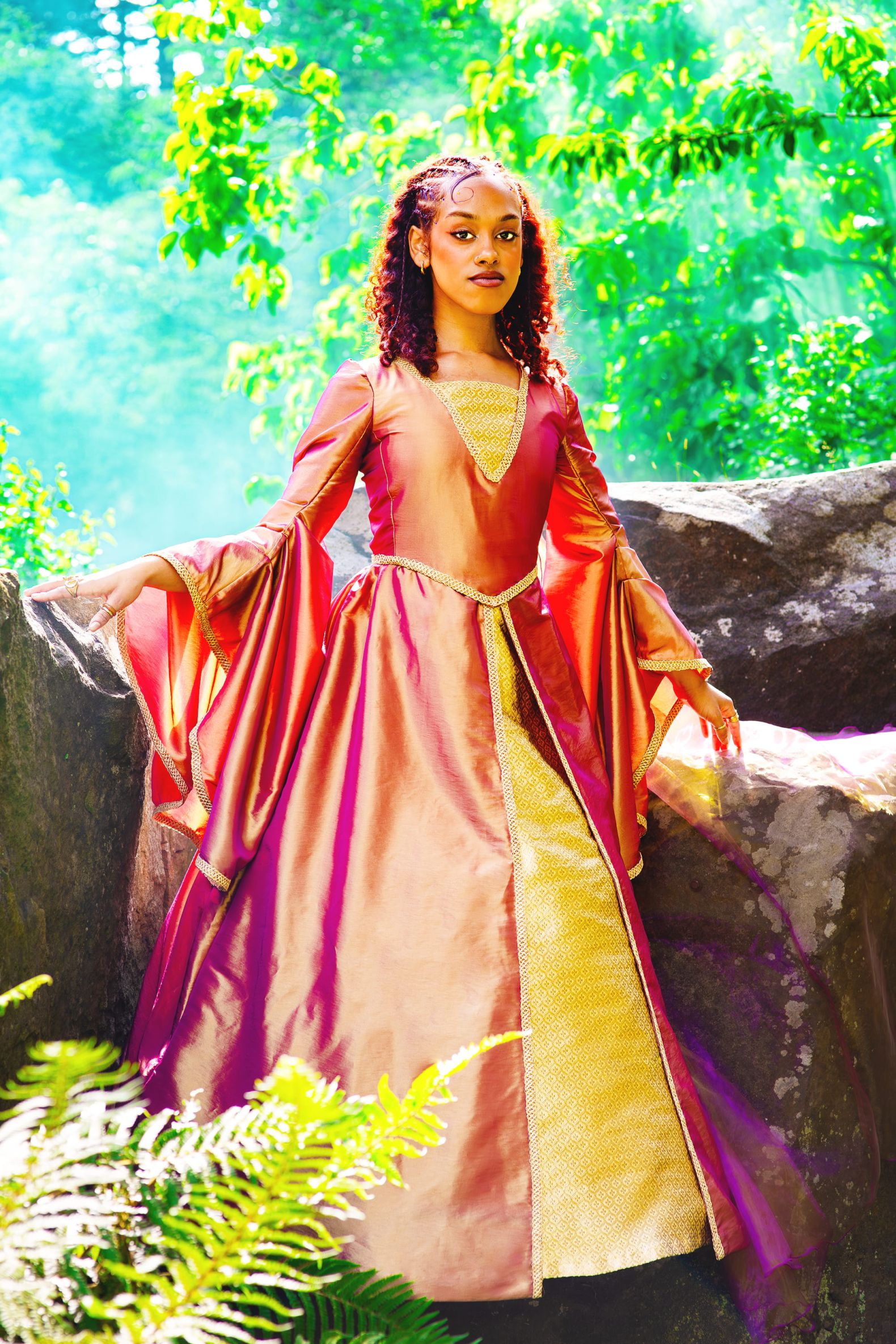 Robin Hood - the Dukes Park Show in Williamson Park: Marian stood on rocks in a purple and orange gown with green trees in the background