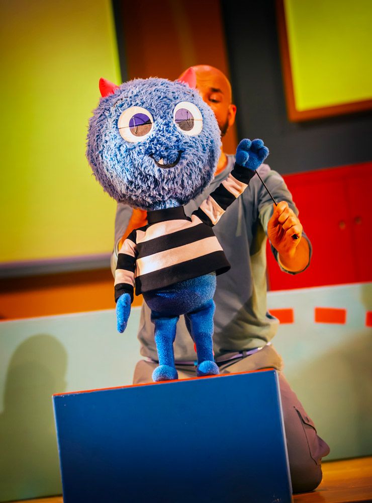 a friendly-looking blue puppet monster, hand raised as if waving.