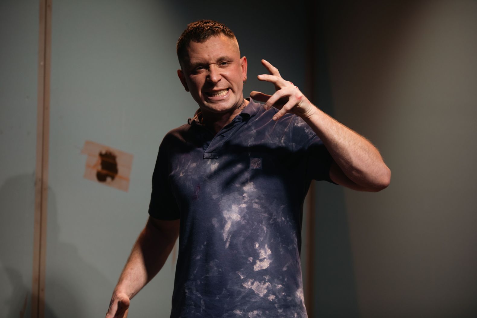 A man, clothes covered in plaster, is expressive and looks frustrated with hand raised in expression.