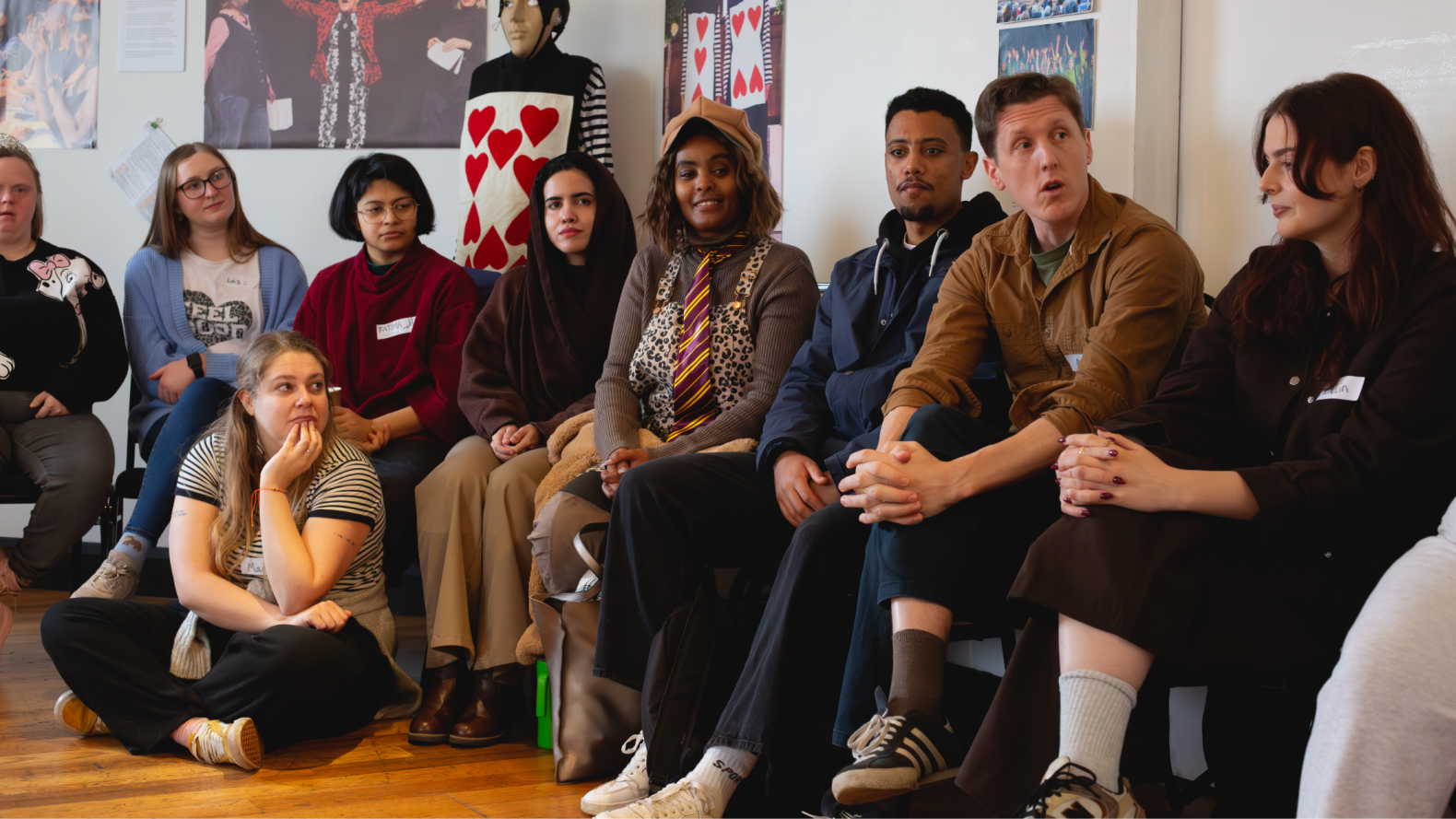 A group of people, from RAIS, Animikki and Members from Unique Kidz, sitting side by side, against the wall. 