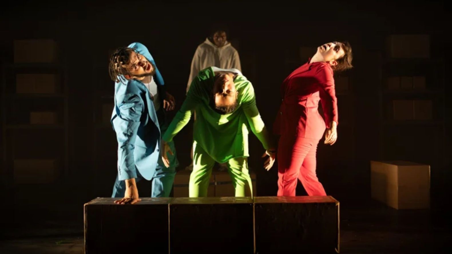 three performers in a circle bending over backwards away from each other.  A 4th performer can be seen in the shaows behind them