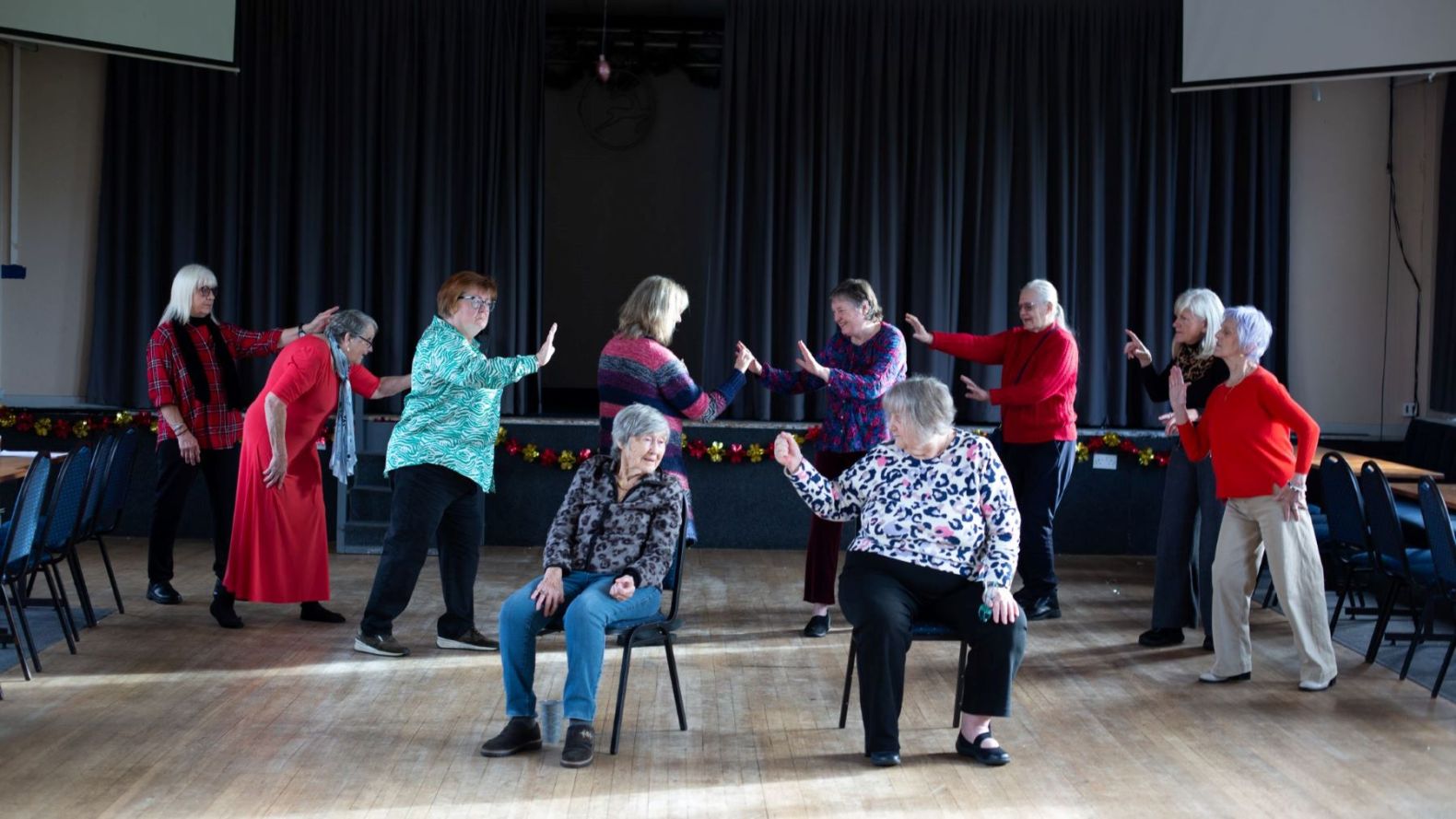 All Morecambe Prime Time members split into two groups, pointing at each other.