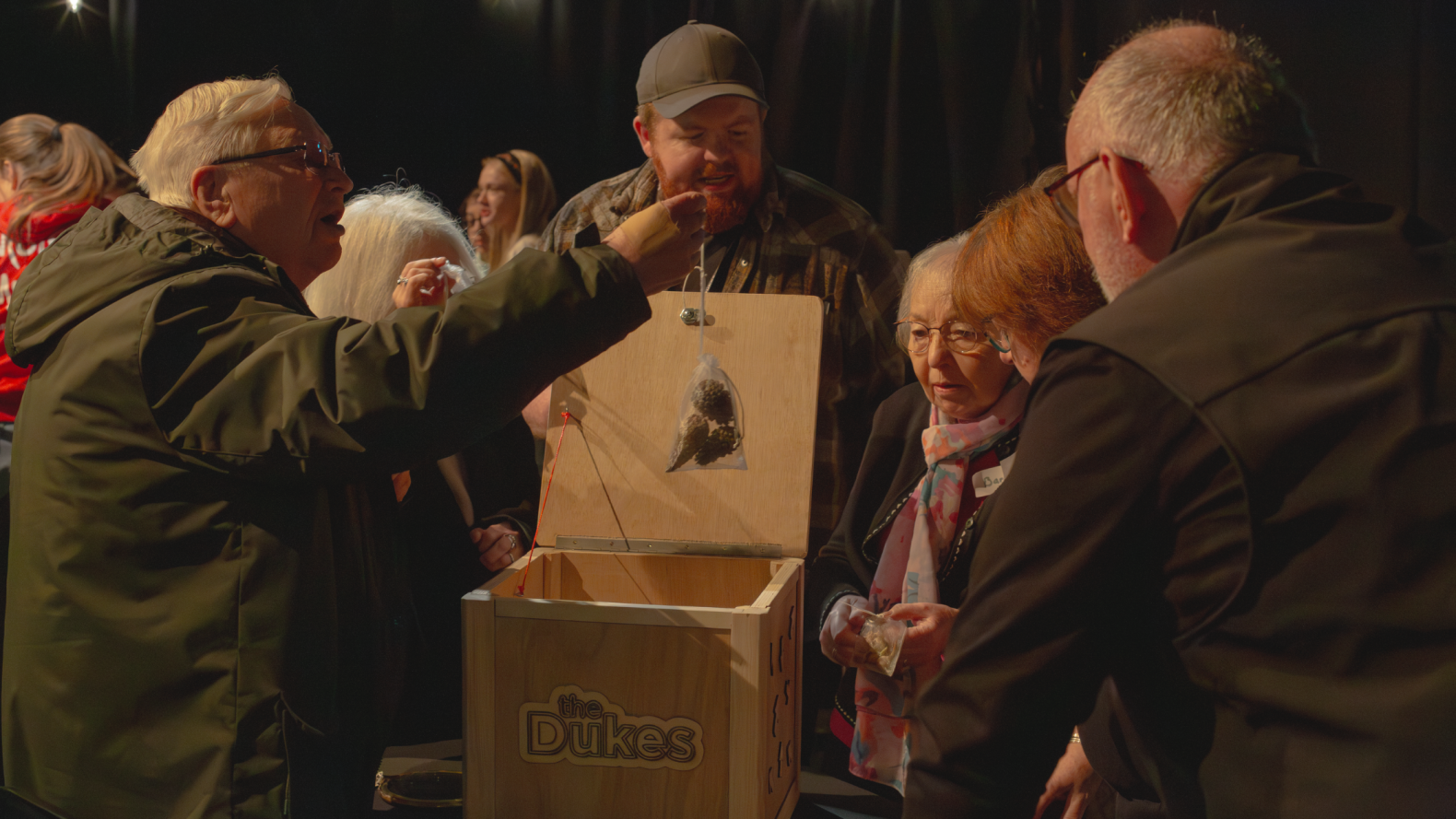 Prime Time members standing around a wooden box. When member is pulling a bag with acorns in them out the box. 