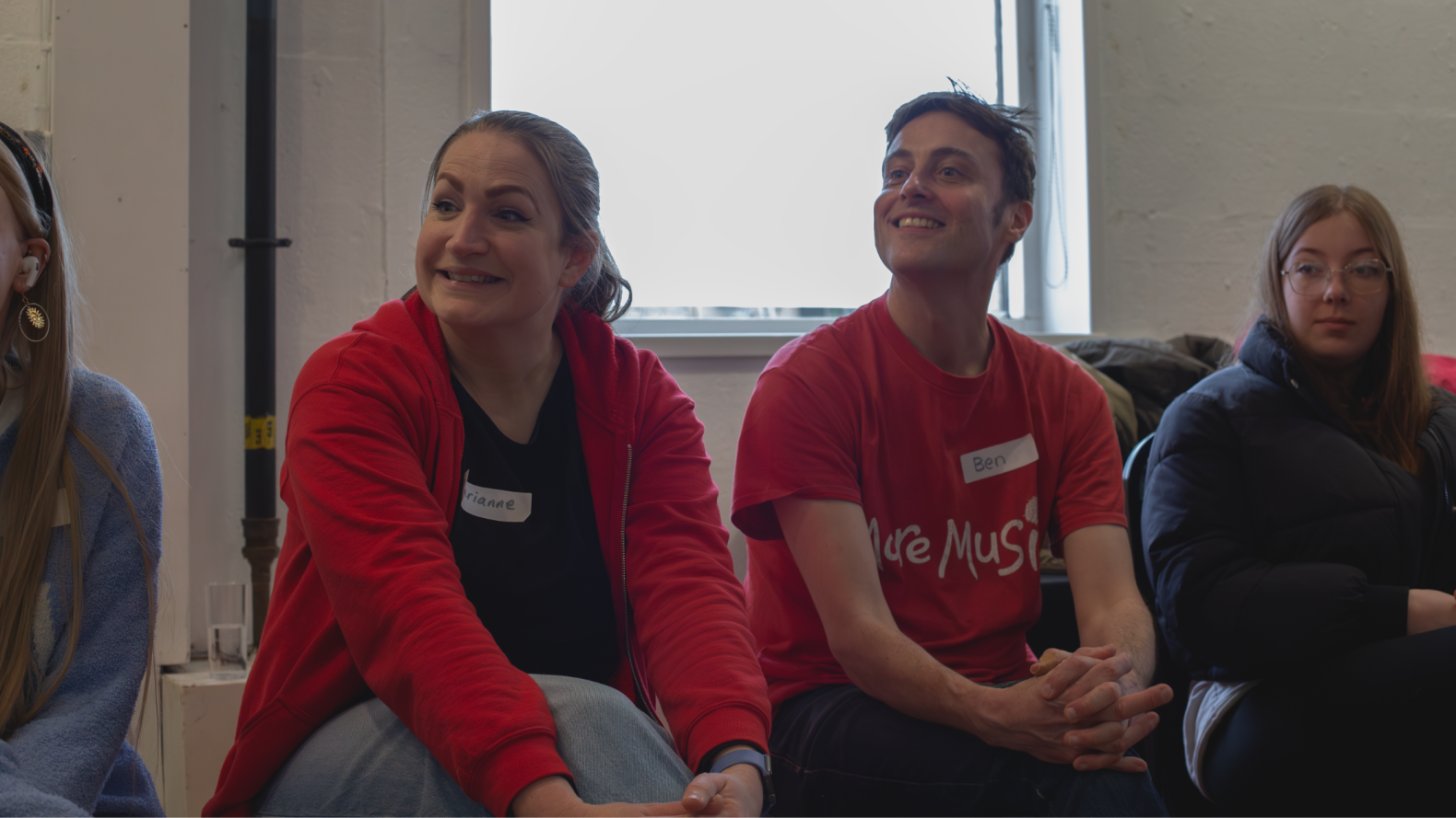A close-up of Marianne and Ben from More Music, wearing red, with both their legs crossed and arms around their knees. 