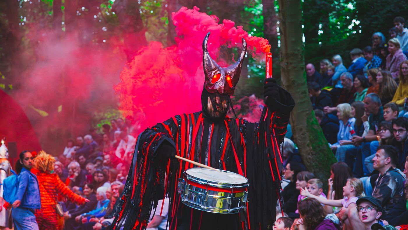 Nigel, the Monkey, (Matthew Ganley) walking towards camera play the drum with one hand and holding a red hand flare, in the other. The Wizard of Oz by the Dukes, photos by Gabi Dawkins.
