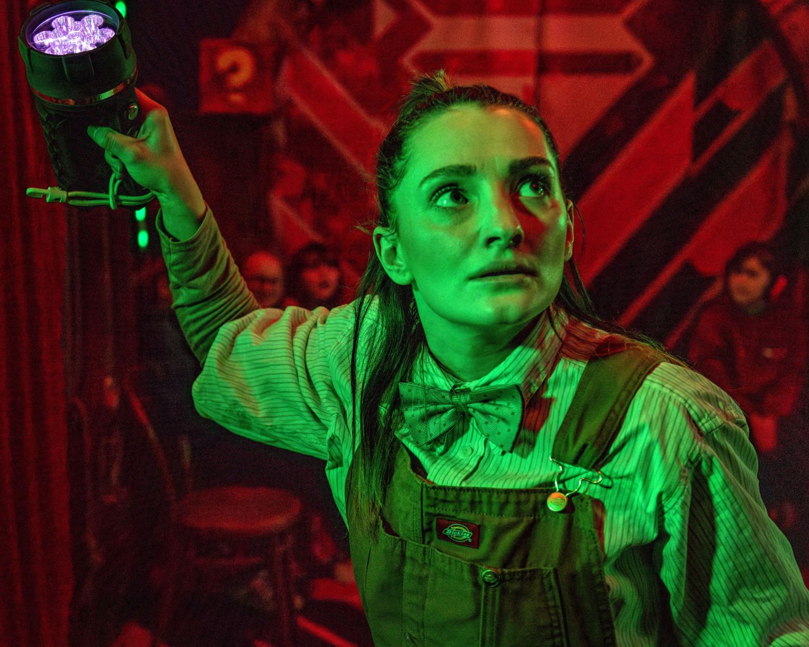 an actor holding a torch above their head, bathed in green light