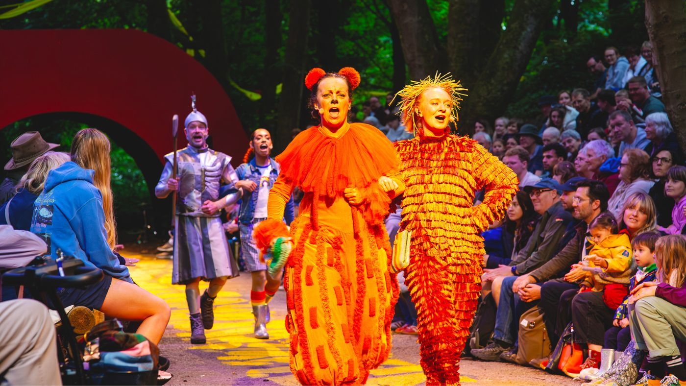 The Lion (Helen Longworth) and Scarecrow (Tori Burgess) with linked arms, skipping down the yellow brick road. Behind them, Tinman (Gareth Cassidy) anf Dorothy (Hope Yolanda), doing the same. The Wizard of Oz by the Dukes, photos by Gabi Dawkins.