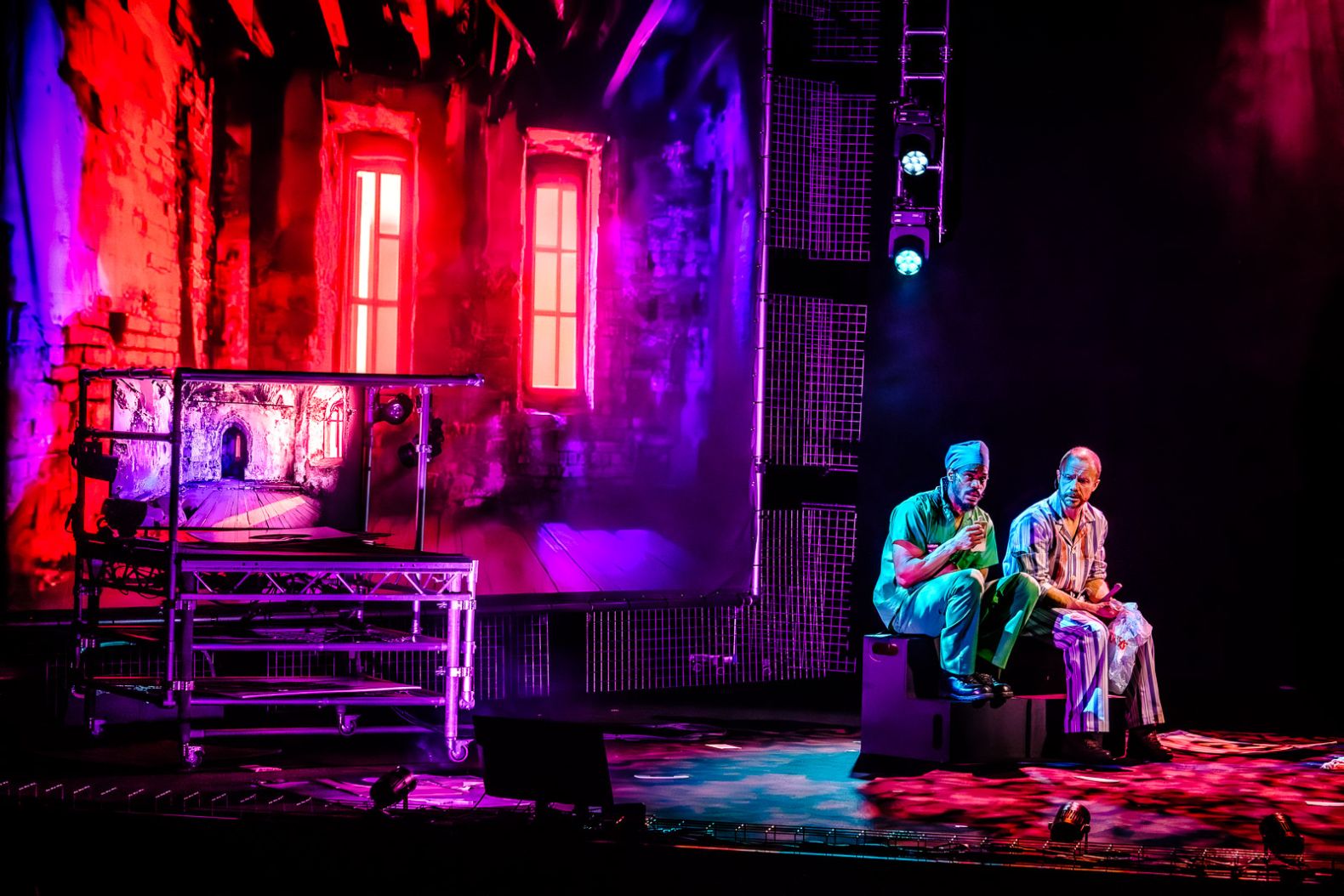 The set of War of the Worlds: a screen with a projection of the inside of a church. The walls and ceilings are exposed. Two actors are sitting on a step box in front of screen.