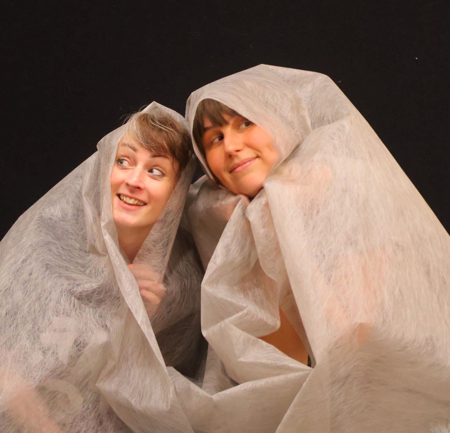 "Warped" promotional image of 2 actors huddled together ,wrapped in white cloth with only their faces showing