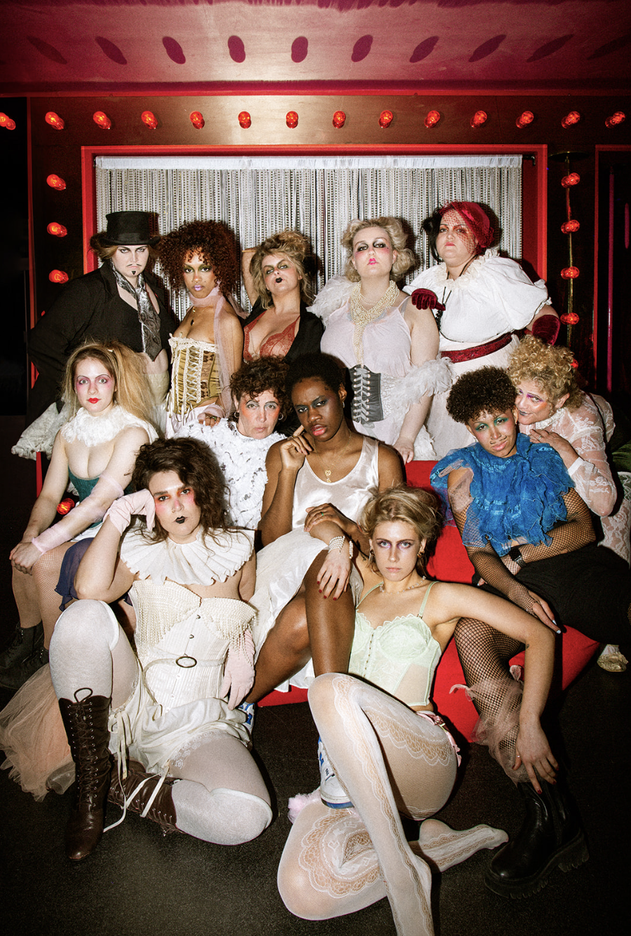 12 Burlesque performers dressed in white lace outfits coupled with blue, red and gold accessories.
