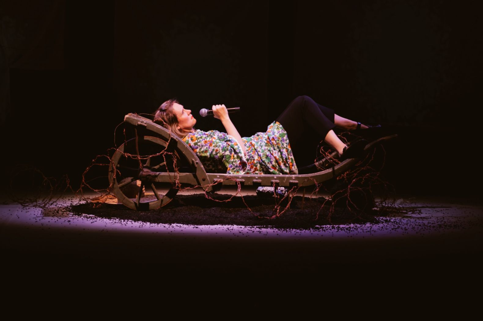 Bryony Kimmings performing in Bog Witch. Bryony is laying down, holding a microphone.