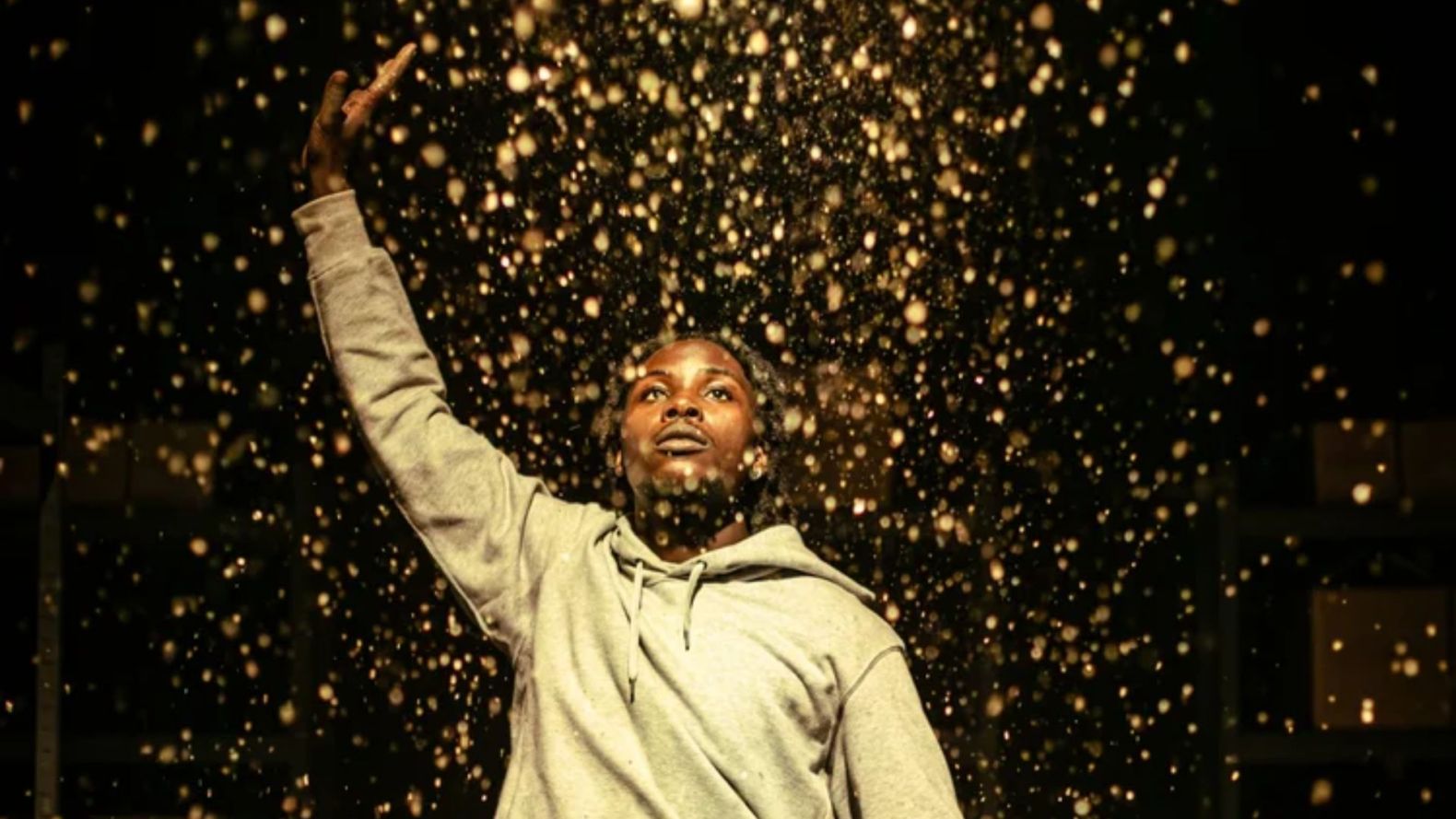 a performer with one arm raised above them, showered in what looks like gold glitter