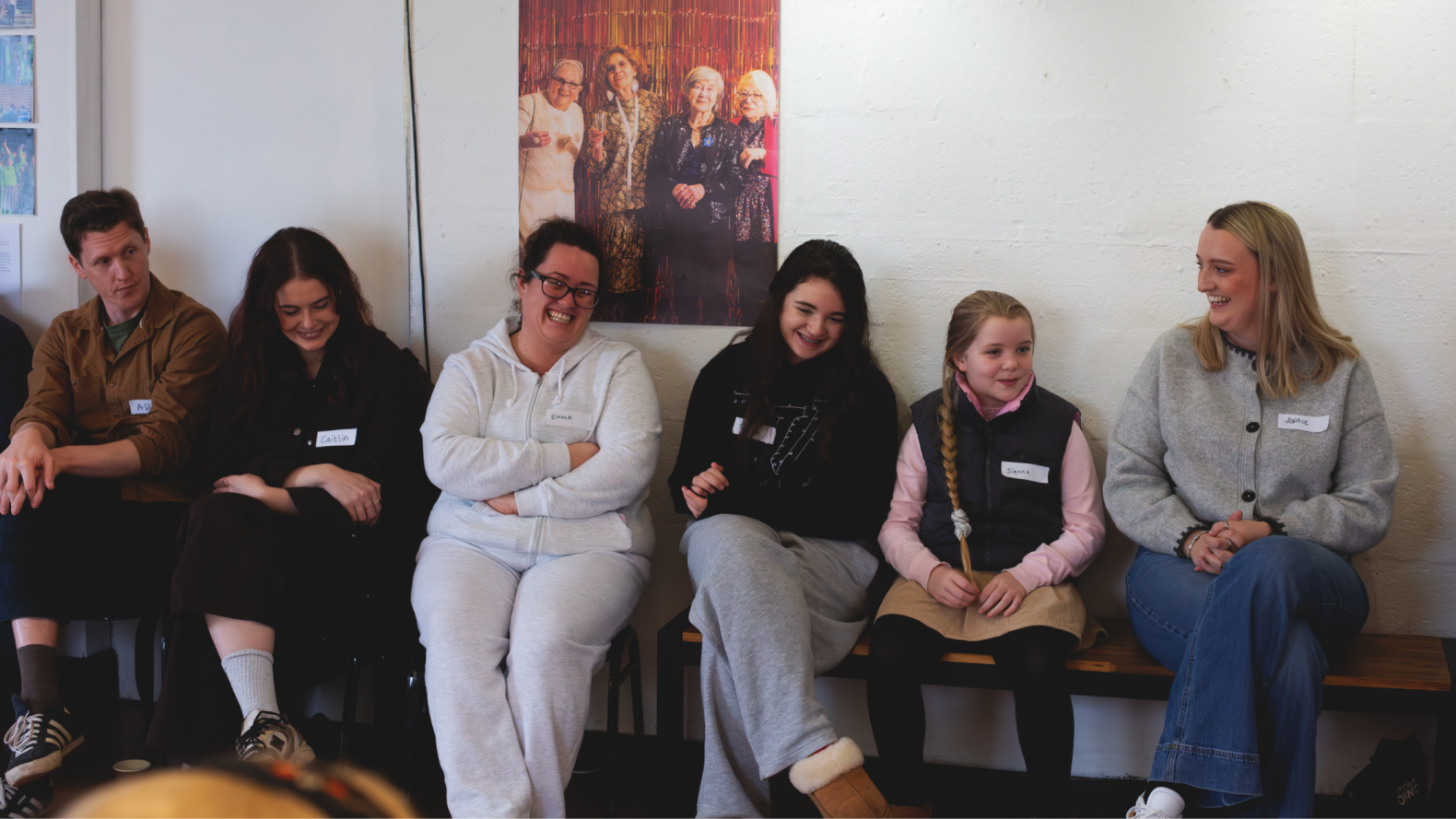 Members of the Traveller Heritage group and Sophie Hodgson sitting on a bench or chair along the wall. On their right are two members from Rais and Animikki.
