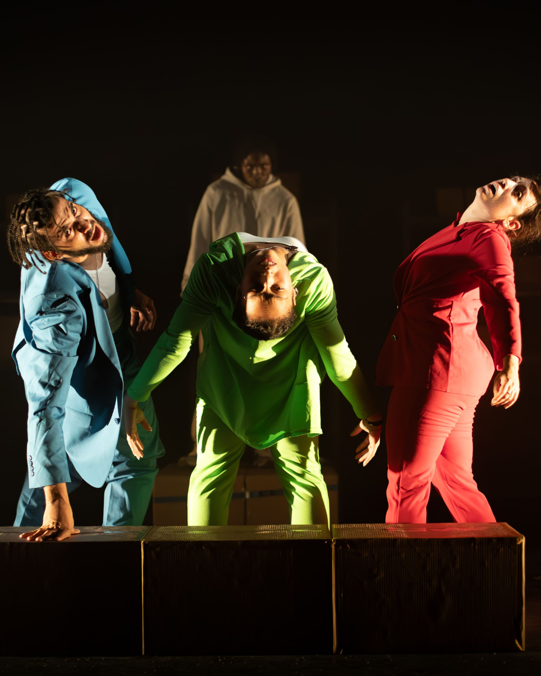 Three performers are on stage dancing. Each are leaning backwards in a seemingly painful contortion
