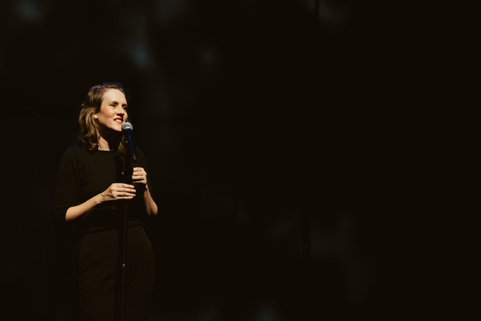 Bryony Kimmings performing in Bog Witch. Bryony is dressed in black with a black background.