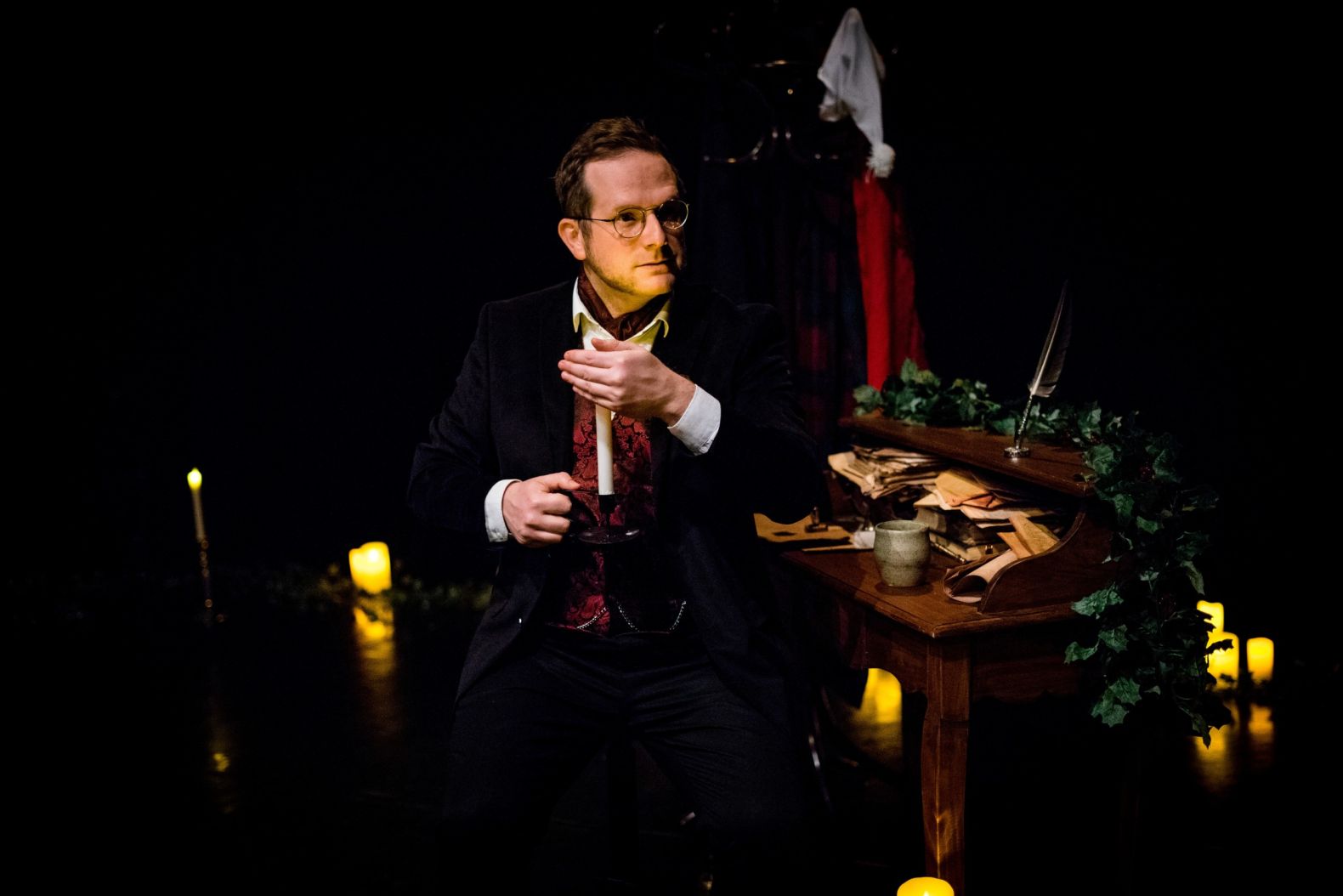 Actor dressed in Victorian attire, sat at a desk holding a candle
