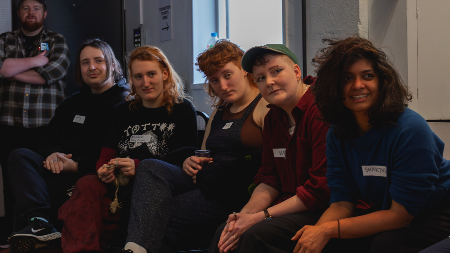 Members of Queer by Gum sitting side-by-side listening to a group sitting across from them. 