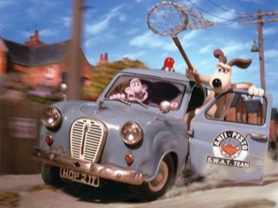 Wallace is driving a car at high speed with Gromit hanging out of the passenger door with a net in hand
