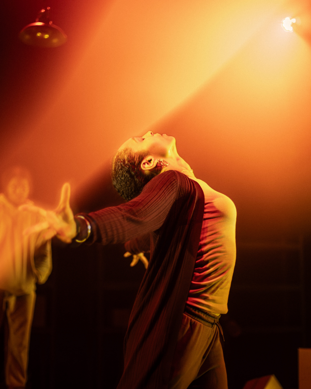 A performer is mid-dance bathing in the light of a theatre light