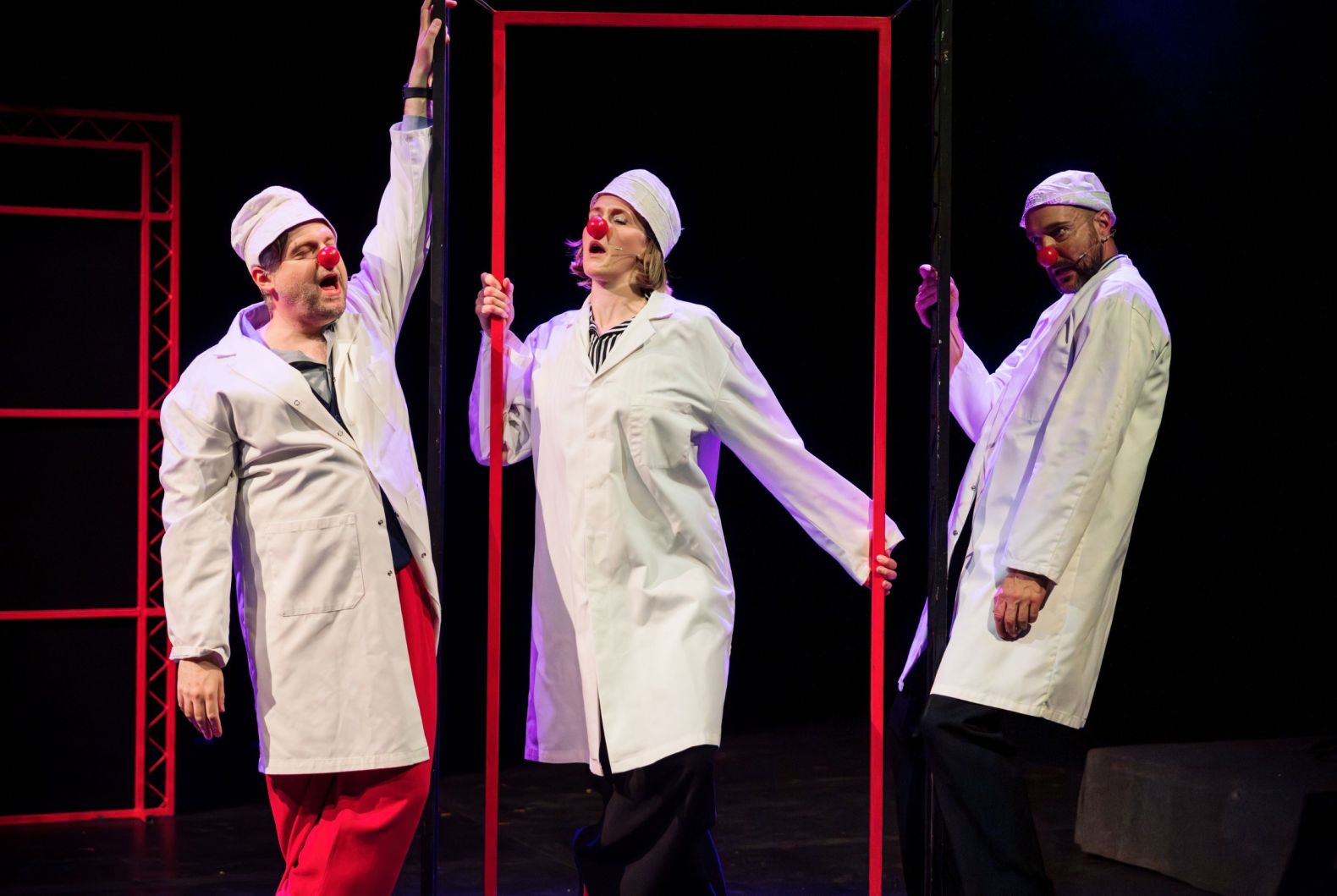 Three actors in white doctor coats, white hats and red clown noses. 