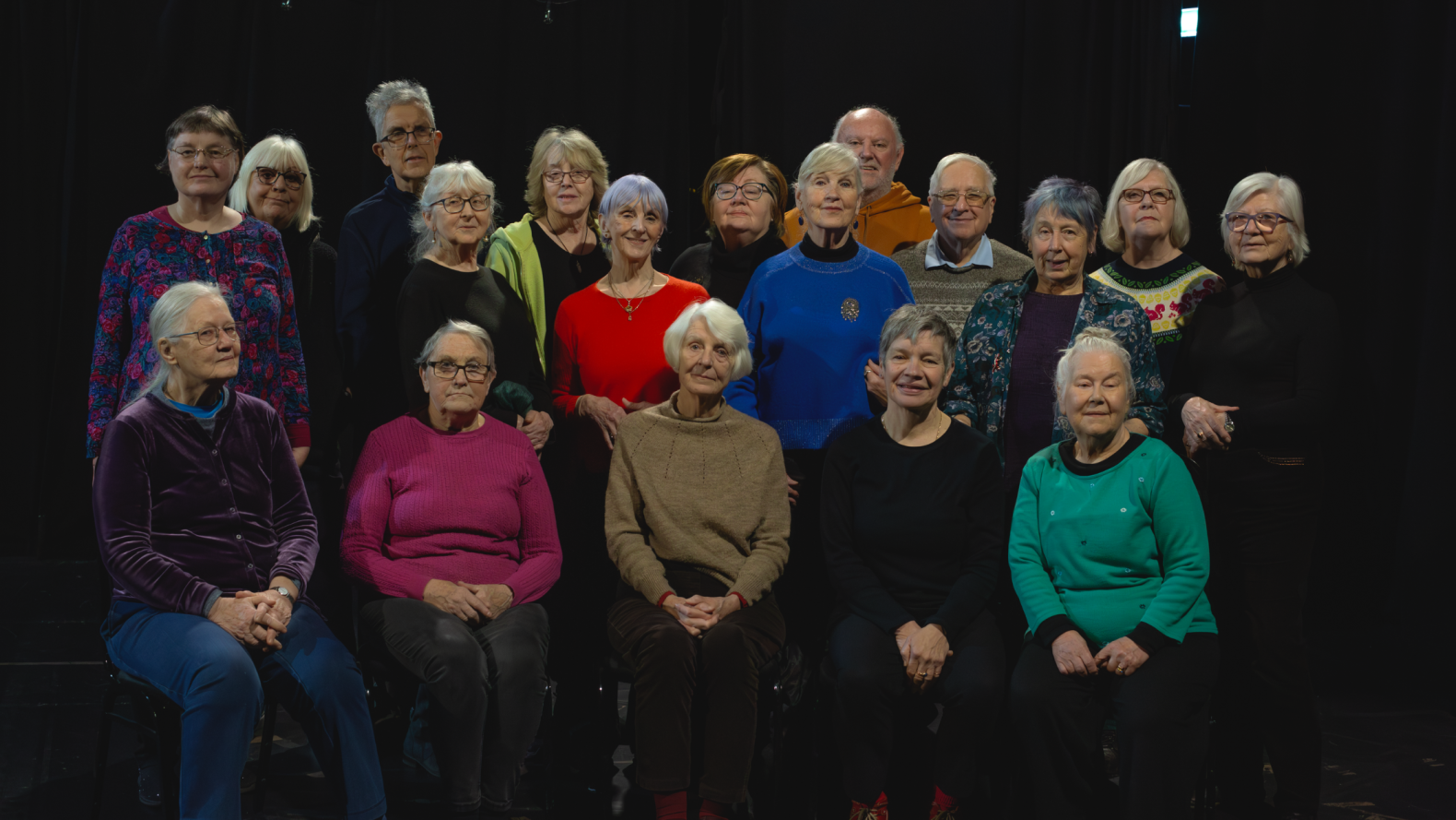 The cast and crew of Prime Time: 18 members who over the age of 60, sitting or standing together as though taking a class photo. They are all smiling with their heads held high. 