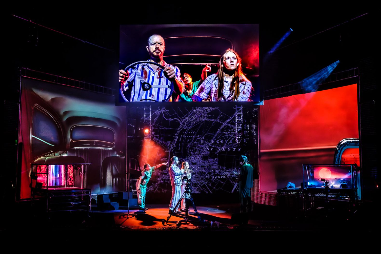 The set of War of the Worlds: Three screens surrounding stage and one hanging above, with projections of the London tube map in the middle, and the inside of a car on the left. The screen above gives the illusion of actors inside car.