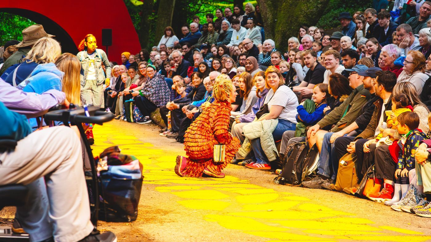 Scarecrow (Tori Burgess), kneeling down, talking to a young person in the crowd. The Wizard of Oz by the Dukes, photos by Gabi Dawkins.