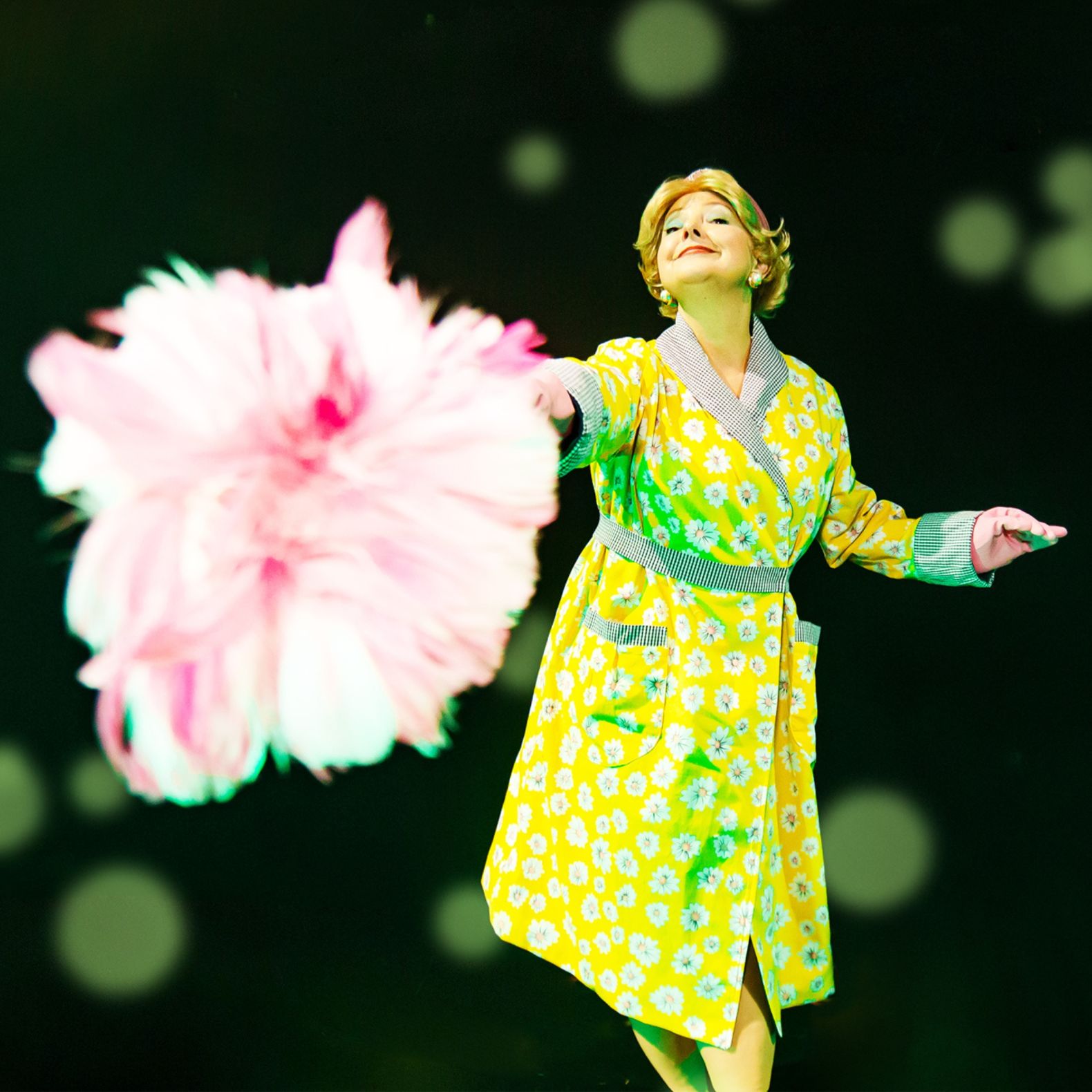 Mrs Driver wearing a yellow inside jacket, poking her pink duster towards the camera