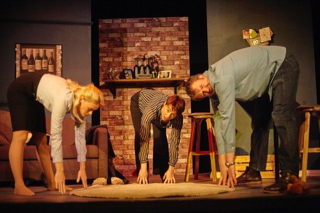 3 actors in a living room setting, bent over touching their toes