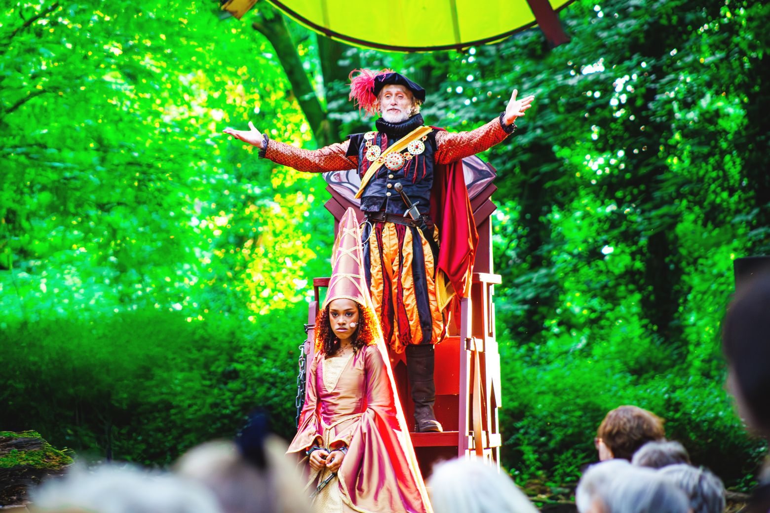 Ian Crowe as the Sheriff addresses the audience standing on a tall wooden throne as Hope Yolanda's Marian stands in front.